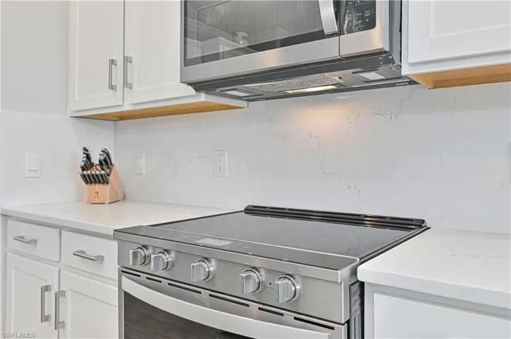 Kitchen featuring appliances with stainless steel finishes, white cabinets, decorative backsplash, and light stone countertops