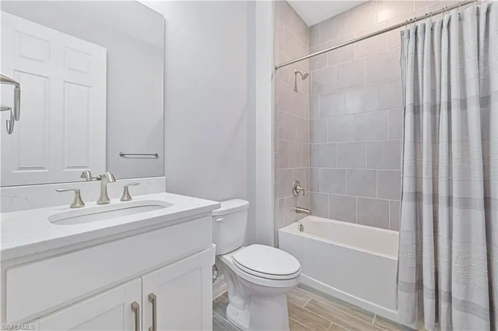 Bathroom featuring vanity, toilet, shower / bath combo with shower curtain, and wood finish floors