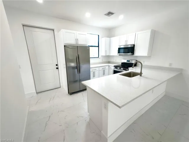 Kitchen with light stone countertops, a peninsula, stainless steel appliances, white cabinets, and recessed lighting