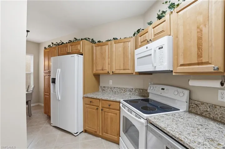 Kitchen featuring white appliances, light stone countertops, and light tile patterned floors