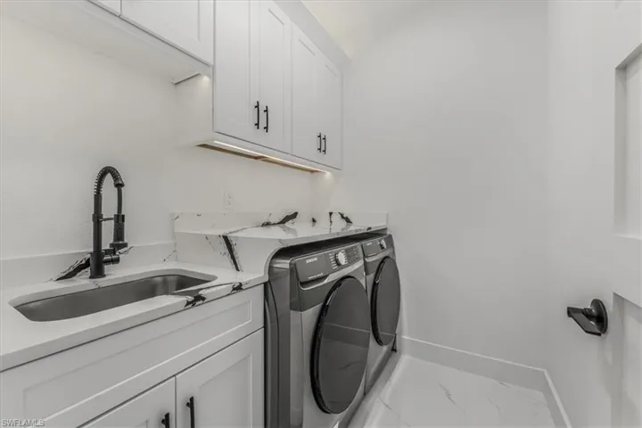 Washroom featuring washer and clothes dryer, cabinet space, and marble look tile flooring