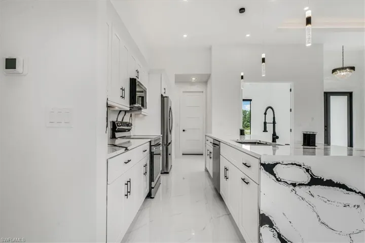 Kitchen with appliances with stainless steel finishes, white cabinetry, recessed lighting, light marble finish floors, and decorative light fixtures