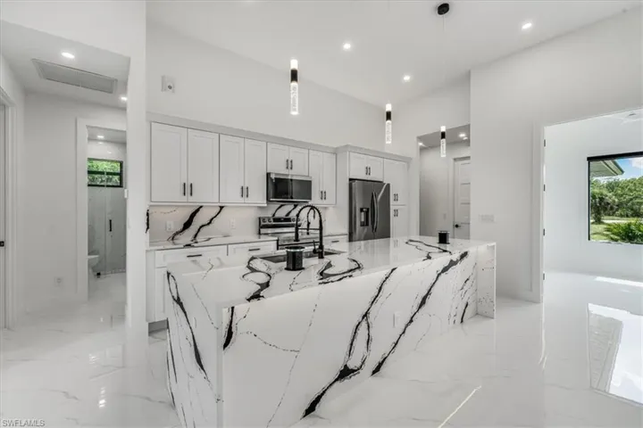 Kitchen featuring appliances with stainless steel finishes, a large island with sink, white cabinetry, recessed lighting, and light marble finish floors