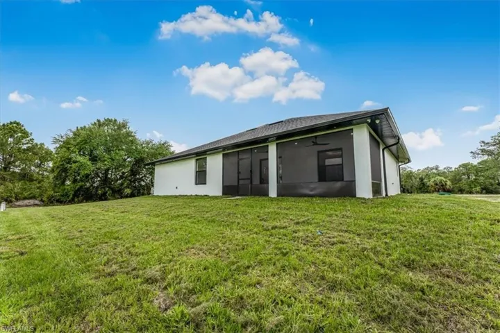 Back of house with a sunroom, a lawn, and stucco siding