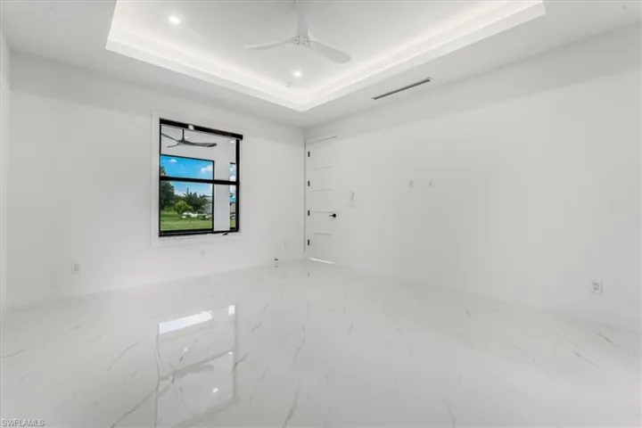 Empty room with a tray ceiling, marble finish flooring, a ceiling fan, and recessed lighting