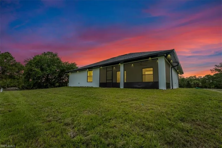 Back of property at dusk featuring stucco siding, a lawn, and a sunroom