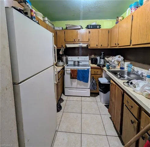 Kitchen with sink, light tile patterned floors, and white appliances