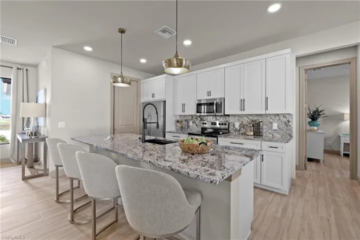 Kitchen with pendant lighting, light wood-type flooring, appliances with stainless steel finishes, light stone counters, and white cabinetry