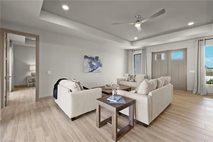 Living room with a raised ceiling, ceiling fan, and light hardwood / wood-style floors