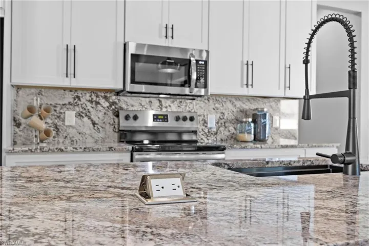 Kitchen with light stone countertops, stainless steel appliances, white cabinetry, and sink