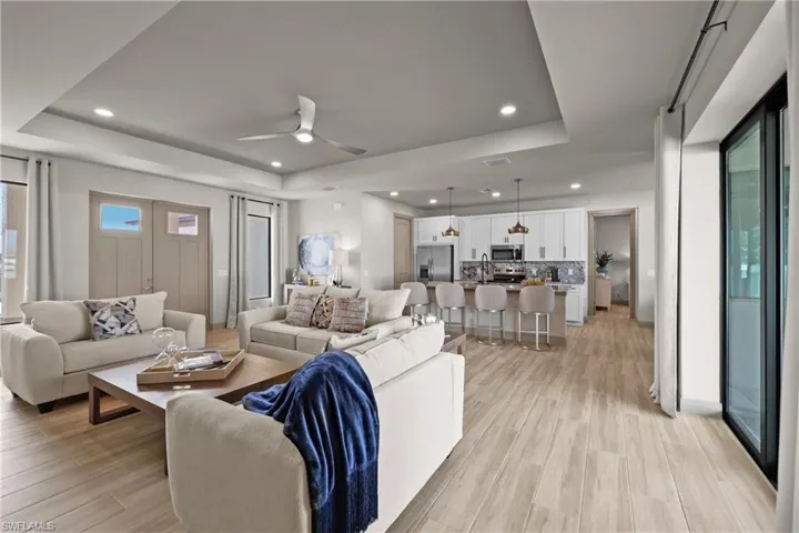 Living room with a tray ceiling, ceiling fan, and light wood-type flooring