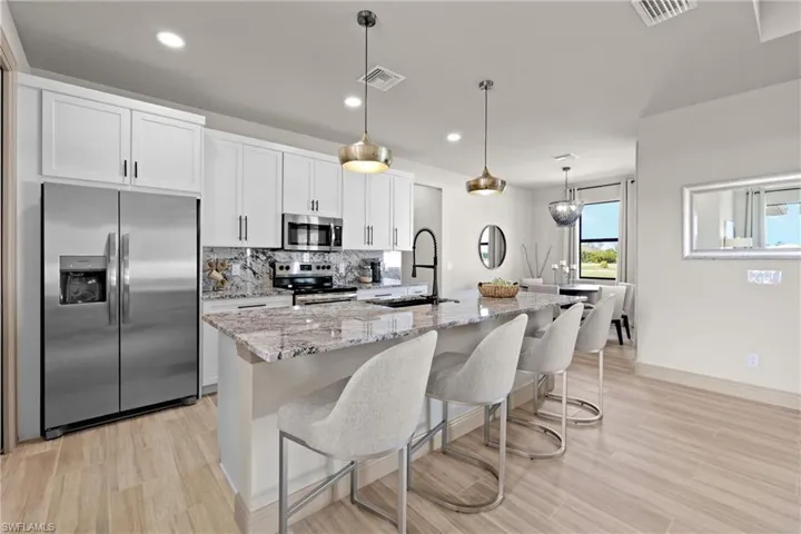 Kitchen featuring sink, stainless steel appliances, pendant lighting, a center island with sink, and white cabinets