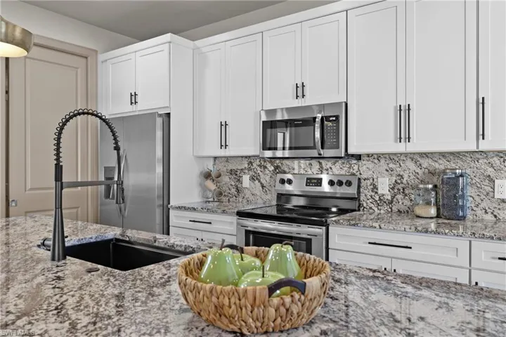 Kitchen with white cabinets, decorative backsplash, light stone countertops, and stainless steel appliances