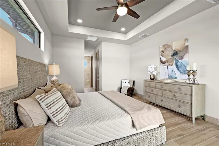 Bedroom with a tray ceiling, connected bathroom, ceiling fan, and light hardwood / wood-style flooring