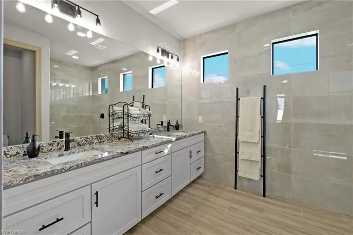 Bathroom with vanity, a tile shower, and tile walls