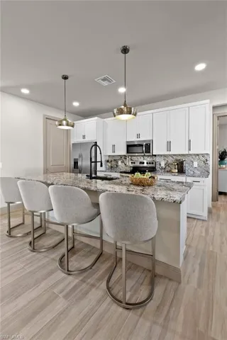 Kitchen with light stone countertops, appliances with stainless steel finishes, decorative light fixtures, light hardwood / wood-style floors, and an island with sink