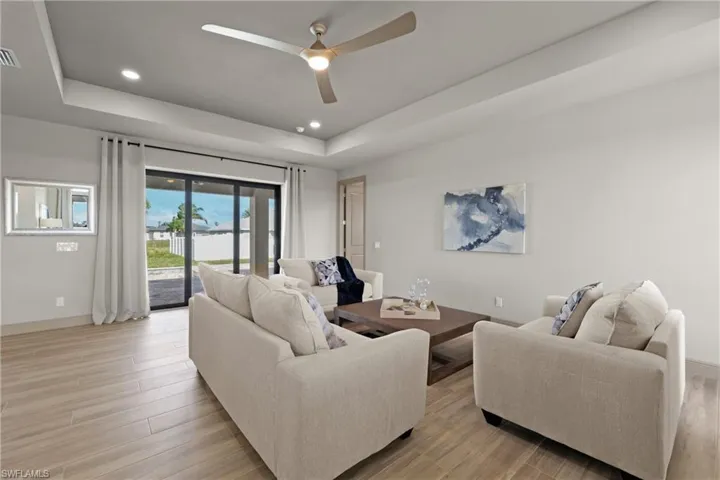 Living room with light wood-type flooring, a raised ceiling, and ceiling fan
