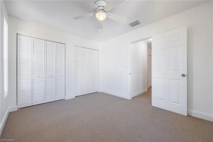 Unfurnished bedroom featuring ceiling fan, light carpet, and multiple closets