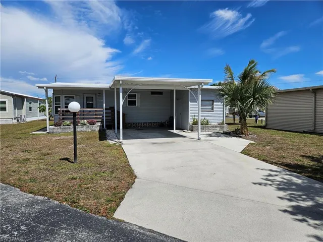 Manufactured / mobile home featuring a front yard, concrete driveway, and an attached carport