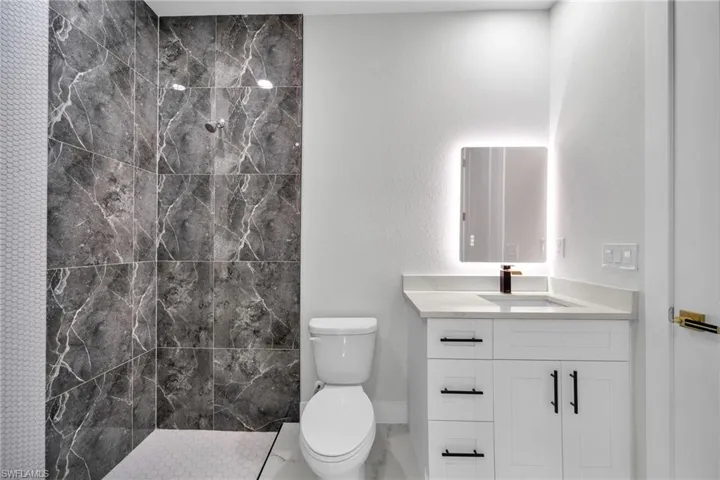 Bathroom with toilet, vanity, and a tile shower