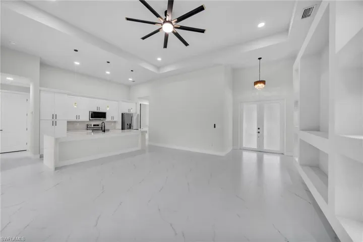 Unfurnished living room featuring ceiling fan, a towering ceiling, light tile patterned floors, and a tray ceiling