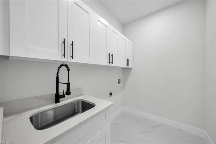 Laundry area featuring light tile patterned flooring, hookup for an electric dryer, washer hookup, cabinets, and sink