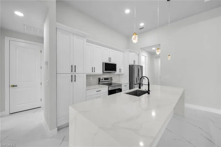 Kitchen with an island with sink, light stone countertops, appliances with stainless steel finishes, decorative light fixtures, and sink