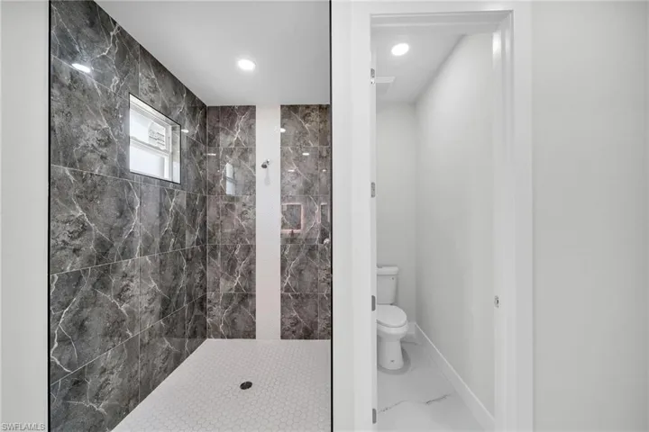 Bathroom with tiled shower, tile patterned floors, and toilet