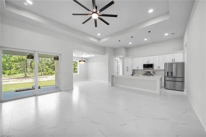 Unfurnished living room with ceiling fan, sink, light tile patterned floors, and a tray ceiling