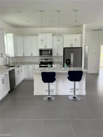 Kitchen with stainless steel appliances, pendant lighting, a kitchen bar, and white cabinetry