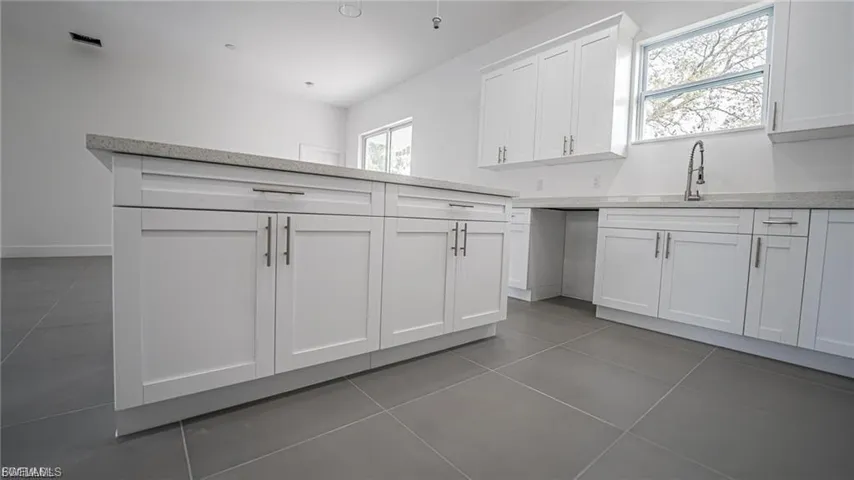 Kitchen featuring light tile patterned flooring, white cabinetry, and light stone countertops