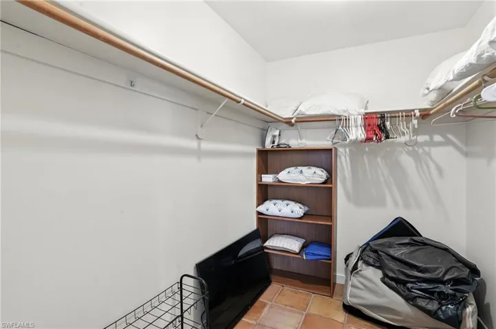 Walk-in closet featuring built-in shelving, wood rods, and tile flooring