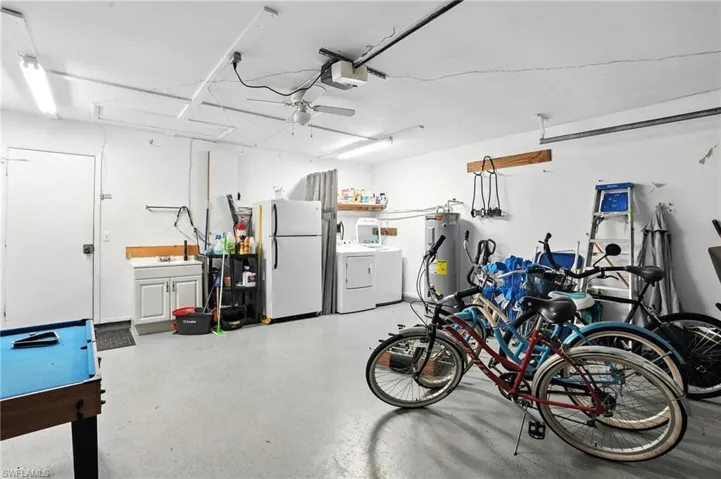 Spacious garage featuring a utility sink, a water heater, overhead fluorescent lighting, a ceiling fan, and a painted concrete floor