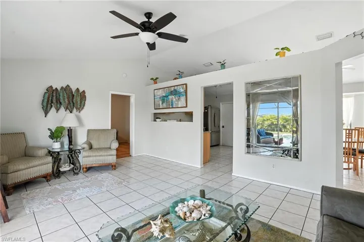 Vaulted ceiling living area featuring tile flooring, a dark-finish ceiling fan with integrated lighting, and a partial wall with an integrated decorative niche