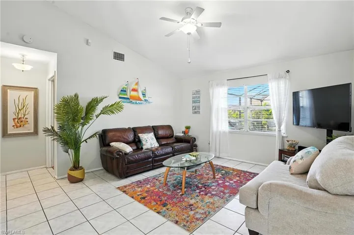 Living area featuring vaulted ceilings, white tile flooring, a ceiling fan with integrated lighting, and a prominent window with blinds