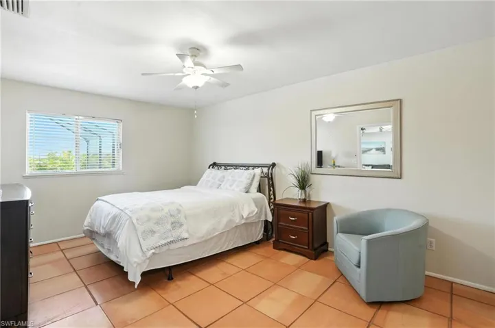 Spacious room featuring terra cotta tile flooring, a window with horizontal blinds, a ceiling fan with integrated lighting, and a wall-mounted mirror with a silver-toned frame