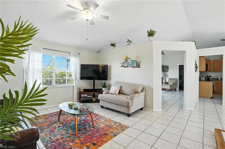 Spacious living area featuring vaulted ceilings, a ceiling fan with integrated lighting, and white tile flooring