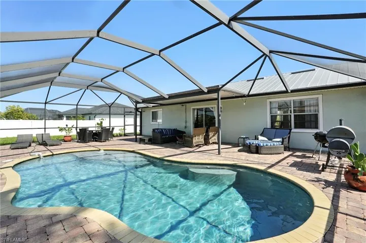 Screened-in outdoor living space featuring a freeform pool with integrated steps, brick paver decking, and a covered patio area with a metal roof
