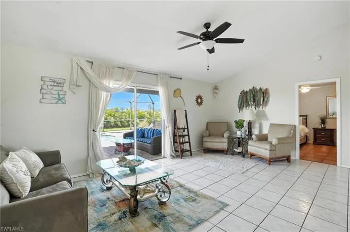 Spacious room featuring tile flooring, sliding glass doors to the exterior, a ceiling fan, and a doorway to an additional room