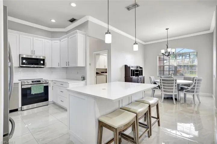 Kitchen featuring stainless steel appliances, ornamental molding, white cabinetry, and pendant lighting