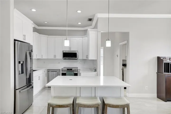 Kitchen featuring a kitchen breakfast bar, stainless steel appliances, crown molding, white cabinetry, and tasteful backsplash
