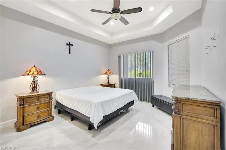 Bedroom featuring a tray ceiling, ceiling fan, and light marble finish floors