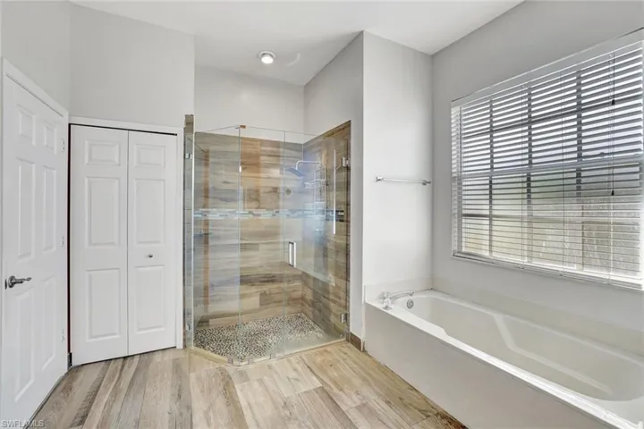 Full bath featuring a shower stall, a bath, light wood-type flooring, and a closet