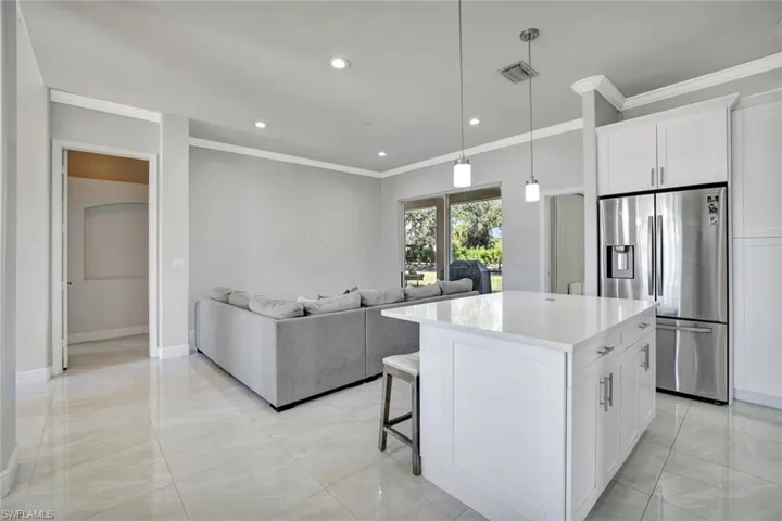 Kitchen with stainless steel refrigerator with ice dispenser, white cabinetry, ornamental molding, a breakfast bar, and pendant lighting