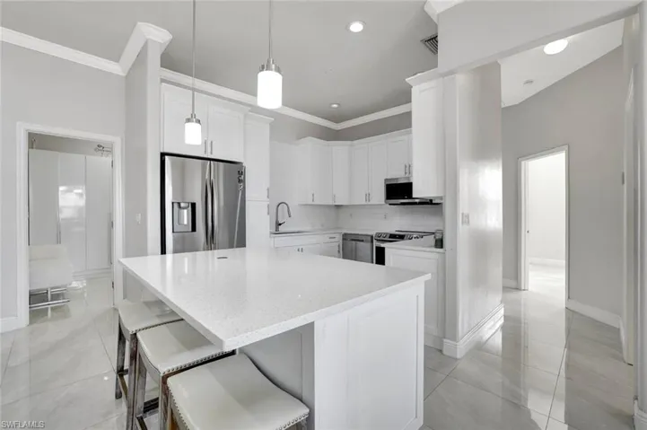 Kitchen with stainless steel appliances, a breakfast bar, white cabinetry, ornamental molding, and light stone countertops