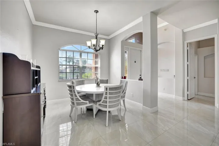 Dining room with ornamental molding, a chandelier, light marble finish floors, and arched walkways