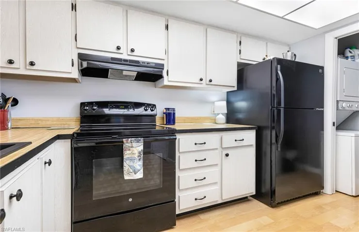 Kitchen featuring white cabinetry, light wood-type flooring, black appliances, stacked washing maching and dryer, and ventilation hood