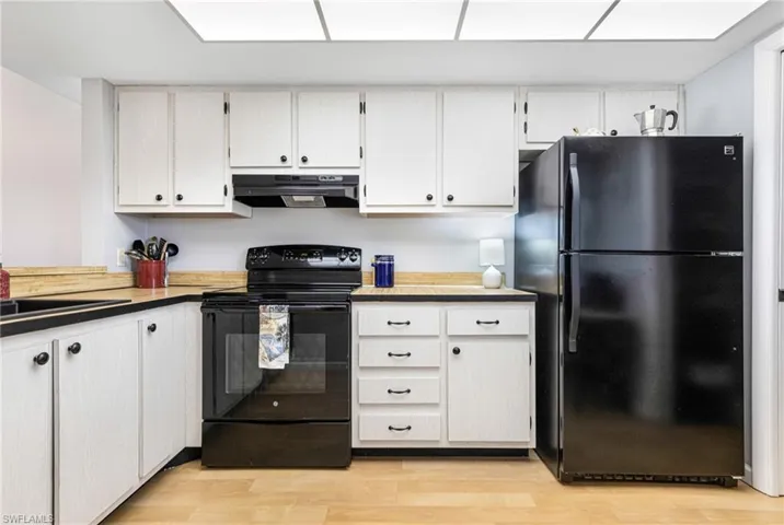 Kitchen with fume extractor, light wood-type flooring, black appliances, sink, and white cabinets