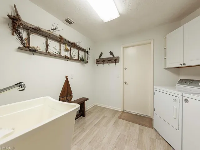 Laundry room featuring a sink, separate washer and dryer, light wood-style flooring, visible vents, and cabinet space