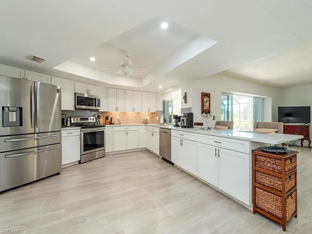 Kitchen with tasteful backsplash, stainless steel appliances, a raised ceiling, visible vents, and a peninsula